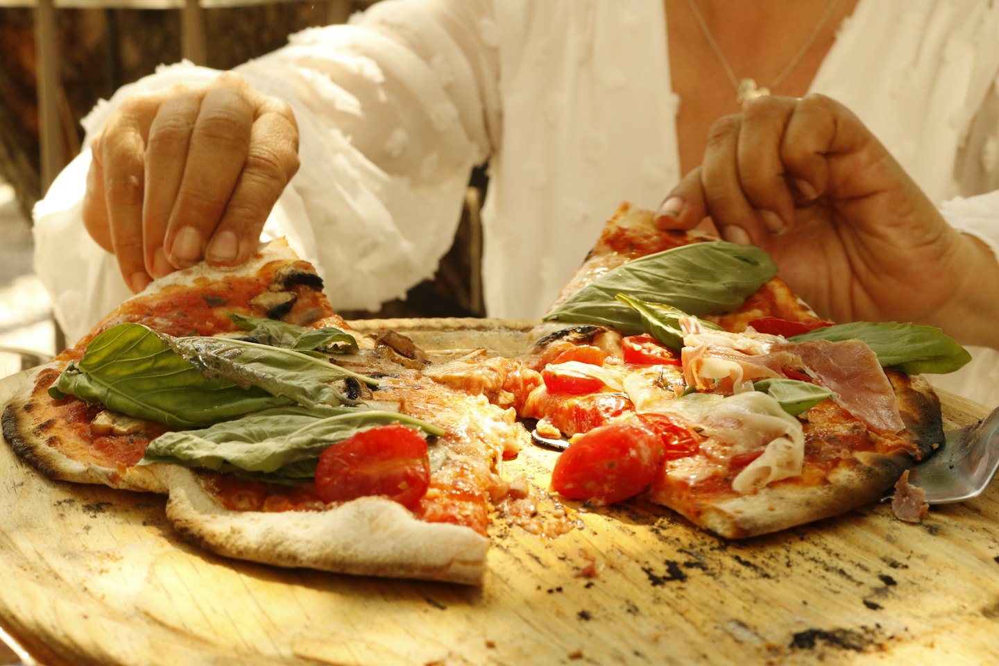 Mani che sollevano fette di pizza da un tagliere di legno.